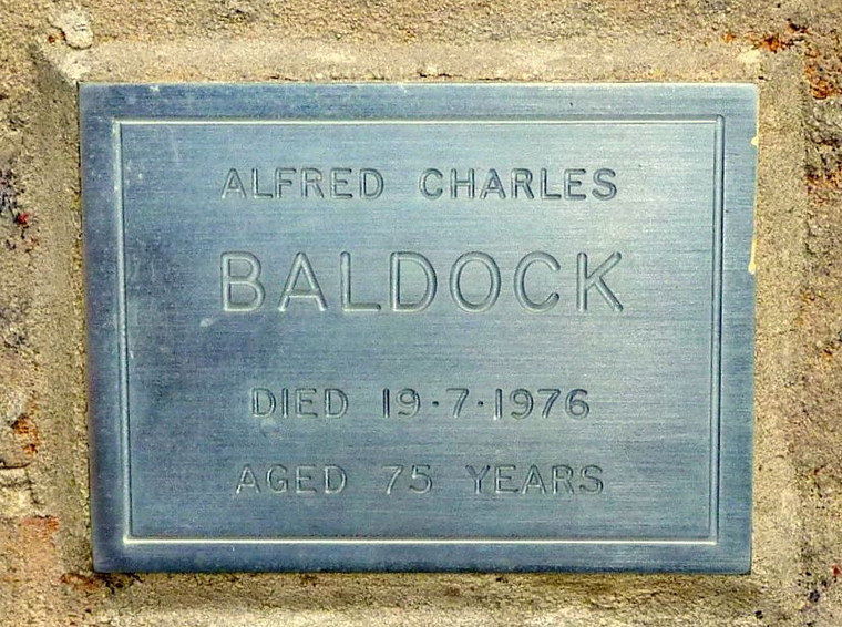 A blue-grey memorial plaque reading "Alfred Charles Baldock, died 19.7.1976, aged 75 years," set into a stone surround.