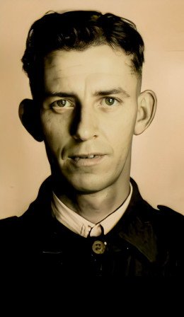A young dark-haired man in a dark military-style jacket, photographed in a head-and-shoulders studio portrait.