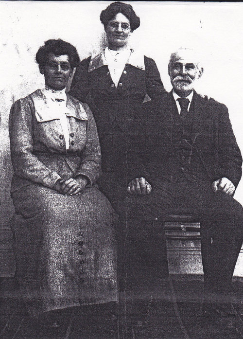 Two women and an elderly bearded man in Edwardian dress, photographed together in a studio.