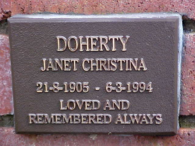 A brown memorial plaque reading "Doherty, Janet Christina, 21-8-1905 - 6-3-1994, loved and remembered always," mounted on a brick wall.