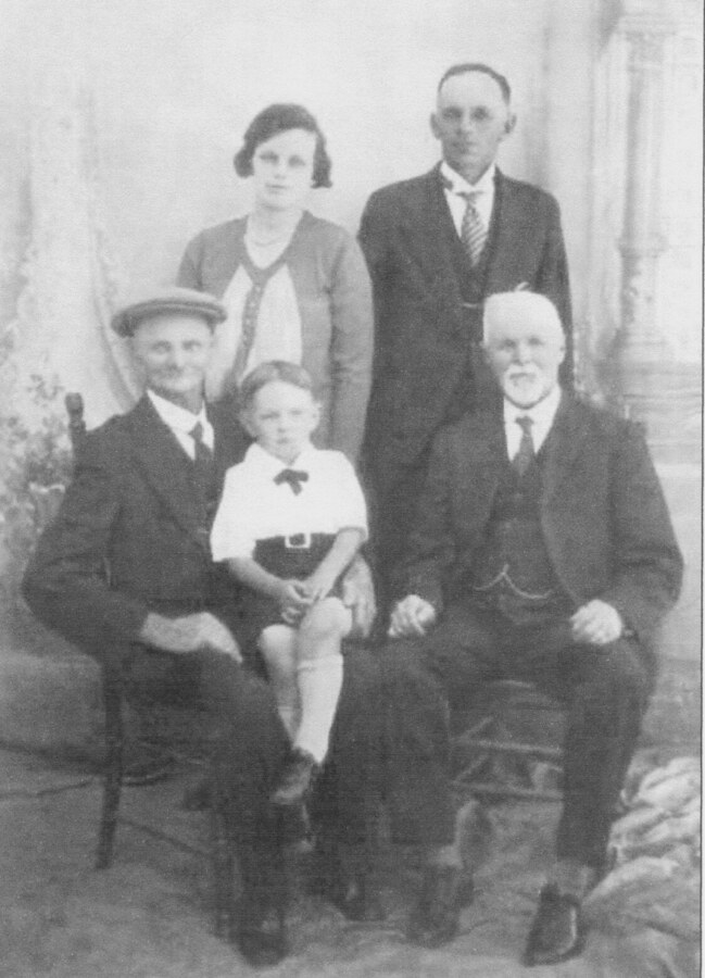 Studio photograph of five people: two elderly men seated with a small boy in a white shirt between them, and a young woman and a man standing behind.