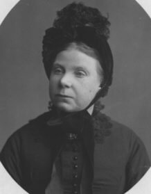 Oval portrait of an older woman in a dark bonnet trimmed with lace and a dark buttoned dress.