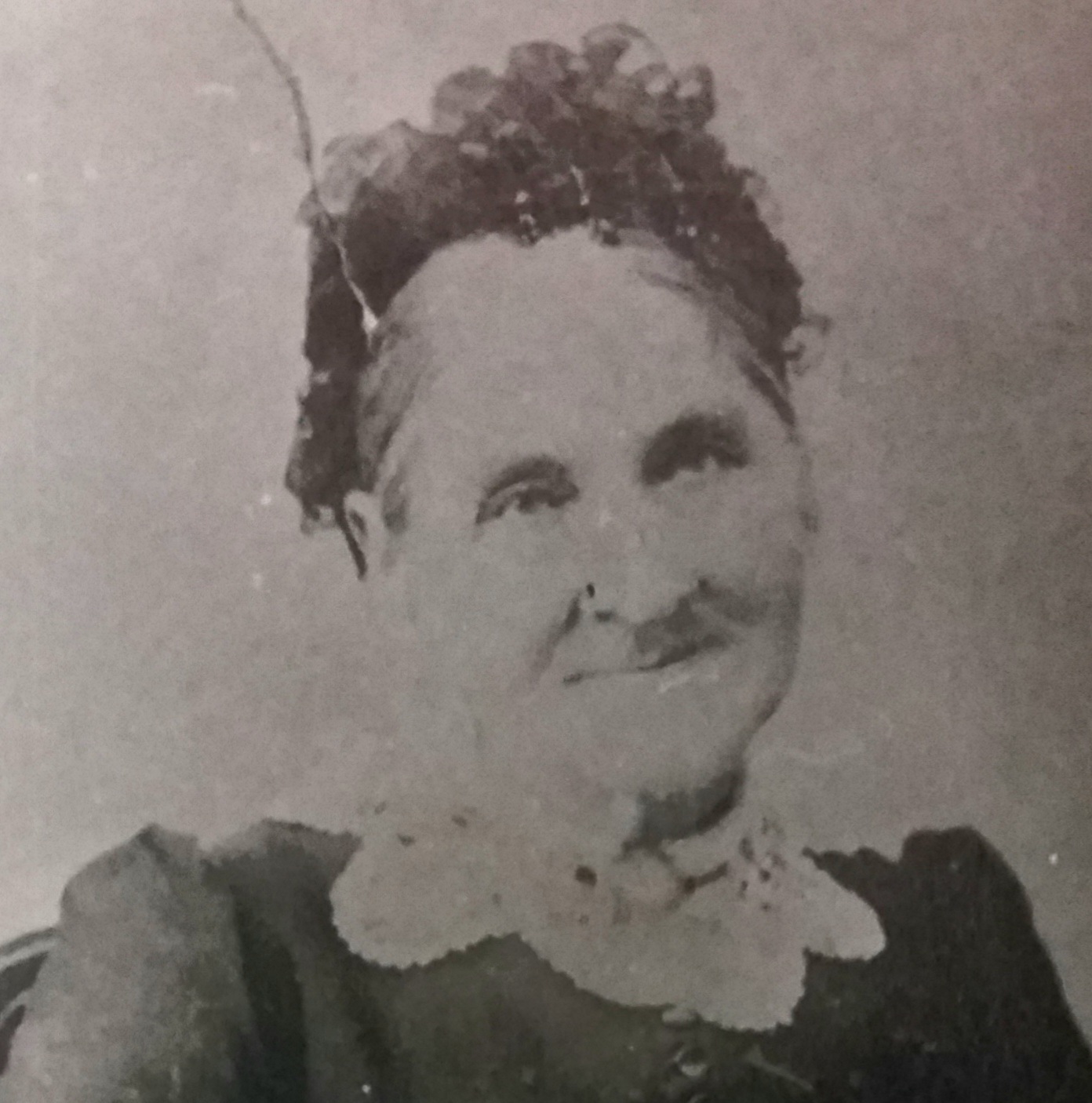 Head-and-shoulders photograph of an elderly woman with hair drawn up, in a dark dress with a broad pale lace collar; the print is faded and lightly foxed.